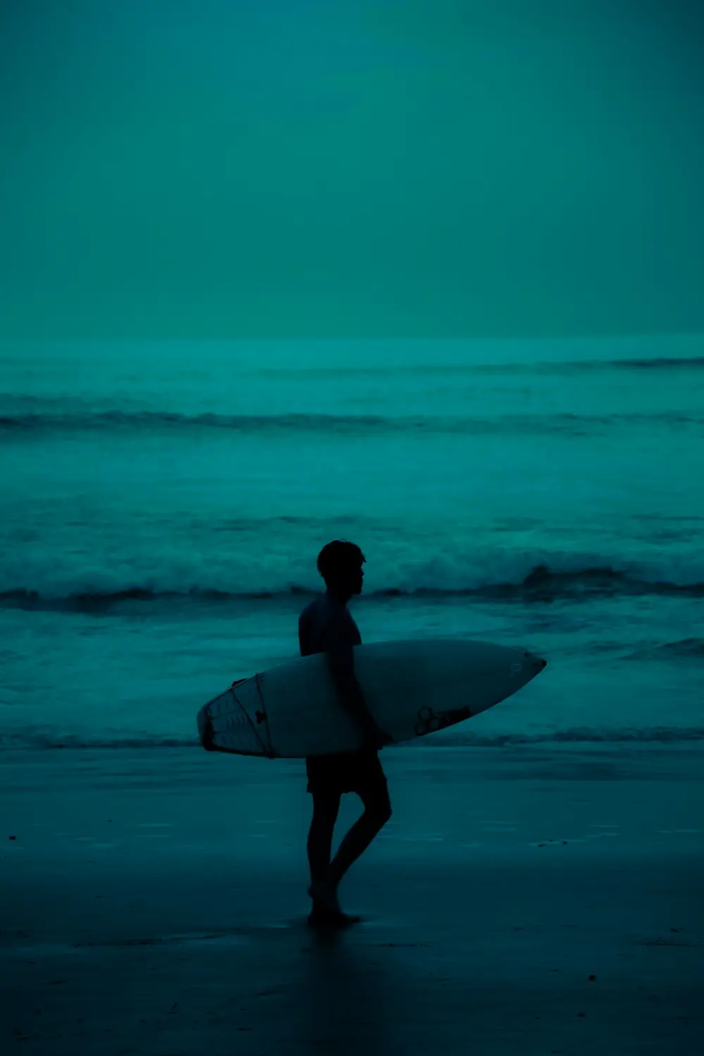 A surfer walking along the shore at Canggu in Bali